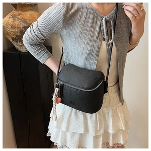 Dettaglio borsa a tracolla nera con texture litchi, zip argento e ciondolo intrecciato
