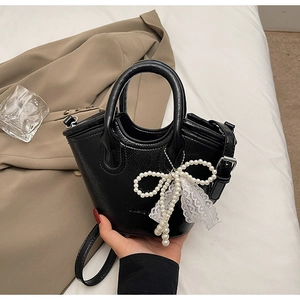Close-up of black leather bucket bag featuring a pearl bow charm and delicate lace trim detail