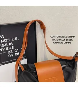 Gros plan sur la bandoulière en cuir marron et le rabat embossé du sac fourre-tout en nylon noir