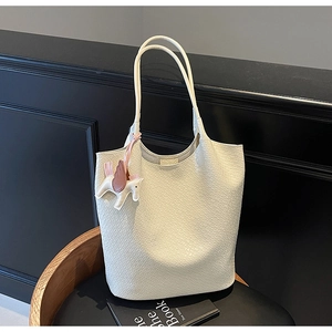 Close-up of cream large tote bag with woven texture and decorative horse pendant