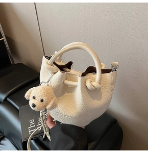 Detail of cream white litchi pattern bucket bag with knotted handle and plush puppy charm