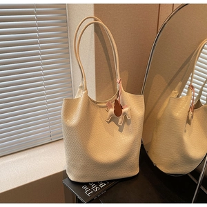 Detail of cream woven tote bag featuring a pegasus charm near a circular mirror