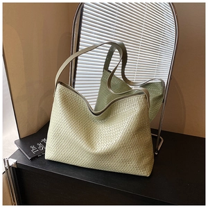 Close-up of light green woven leather hobo tote bag texture on a dark studio table