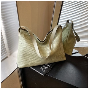 Close-up of a light green woven tote bag with a wide shoulder strap in a cozy home setting