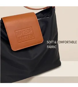Détail du cabas en nylon noir avec rabat en cuir marron et logo de marque embossé
