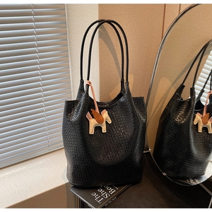 Detail of black woven tote bag with a white horse charm in a stylish setting