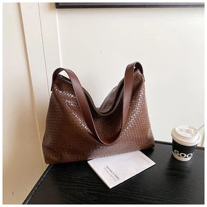 Close-up of the dark brown woven texture and wide shoulder strap on a large leather hobo bag