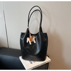 Detail of black woven texture tote bag featuring a decorative pegasus horse charm