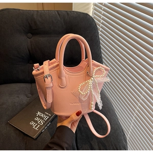 Detail of pink leather bucket bag with pearl bow accessory and elegant textured surface