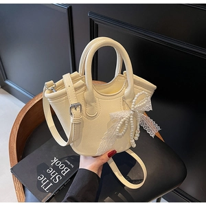 Detail view of cream white bucket bag with elegant pearl and lace bow charm detail