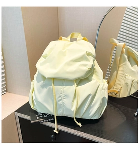 Detail of cream pleated nylon backpack showing side pocket and drawstring closure design