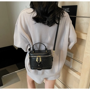 Detail of black woven texture box bag with gold double zippers and fashion tag on model