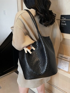 Elegant black woven tote bag with horse charm shown on model in a cozy interior