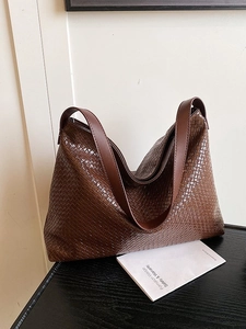 Large dark brown woven leather tote bag with thick shoulder strap on black table