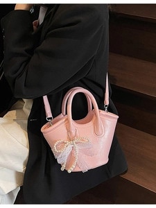 Pink bucket bag with pearl bow accessory and adjustable strap shown on a model
