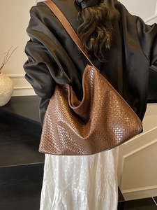 Brown woven large capacity tote bag worn by a model in a minimalist interior setting
