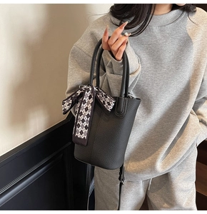 Detail of black pebbled leather bucket bag featuring a decorative checkerboard scarf wrap