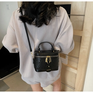 Detail of black PU leather bucket bag with woven texture and gold zipper worn by model