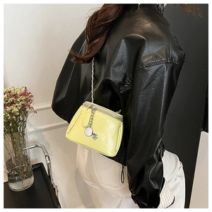 Détail du sac bandoulière en cuir verni jaune avec chaîne et breloque en argent