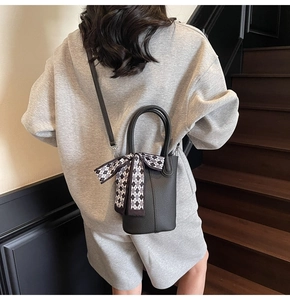 Detail of black pebbled leather bucket bag with a checkered silk scarf and long strap