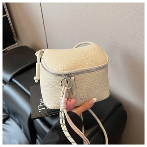 Dettaglio della borsa in pelle color crema con trama a grana e ciondolo a forma di cuore