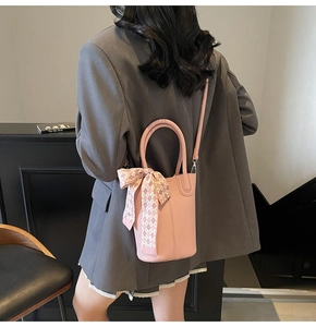 Pink lychee grain bucket bag with silk scarf detail worn over a dark grey blazer