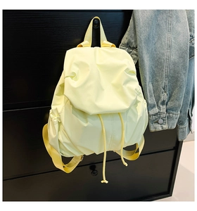 Detail of light yellow nylon backpack hanging on black cabinet with denim jacket background