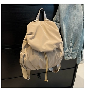 Detail of beige nylon backpack with drawstring closure hanging on a black wooden dresser