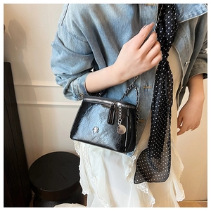 Détail d'un sac seau noir brillant texturé avec logo fleur et chaîne en métal argenté