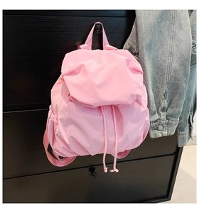 Pink pleated nylon backpack hanging on a vintage cabinet with a denim jacket background