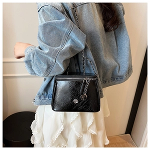 Détail du sac seau noir brillant avec relief camélia argenté et bandoulière chaîne