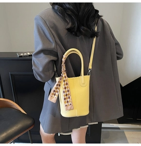 Detail of yellow lychee leather bucket bag with decorative scarf and shoulder strap