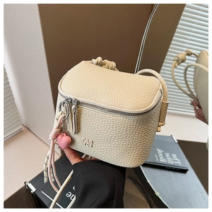 Dettaglio borsa a scatola in pelle beige con logo in rilievo e ciondolo a cuore