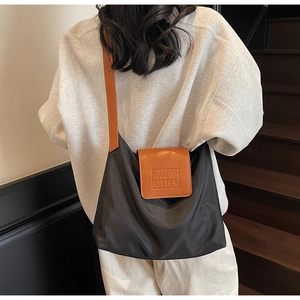 Détail du sac cabas noir avec rabat en cuir marron et logo embossé élégant