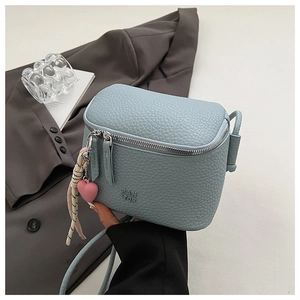 Dettaglio borsa box azzurra con trama litchi e logo goffrato su blazer grigio