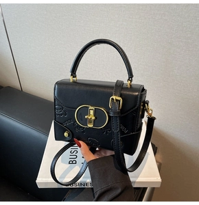 Detail of black crossbody bag featuring embossed bear patterns and gold oval buckle