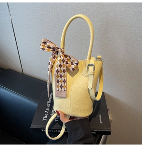 Detail of yellow lychee leather bucket bag with decorative scarf and metal buckle