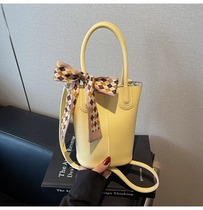 Detail of bright yellow bucket bag with lychee texture and plaid decorative scarf handle