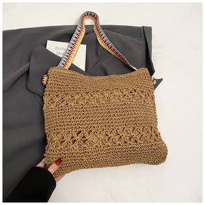 Détail d'un sac cabas en paille avec motif floral ajouré et bandoulière ethnique colorée