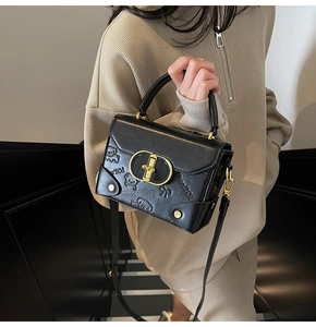 Detail of black crossbody bag with embossed bear pattern and golden ring buckle