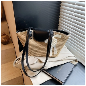 Detail of straw woven tote bag with black leather trim and pearl bow charm accessory