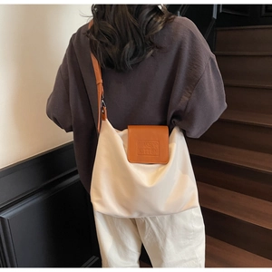 Détail du sac cabas beige avec rabat en cuir marron et logo de la marque embossé