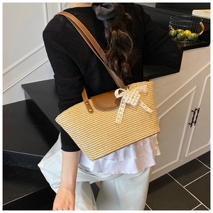 Detail of woven straw tote bag with brown leather straps and pearl bow accessory