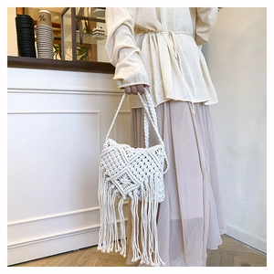 Detail of bohemian white cotton woven bag featuring intricate hollow knit and long fringe trim
