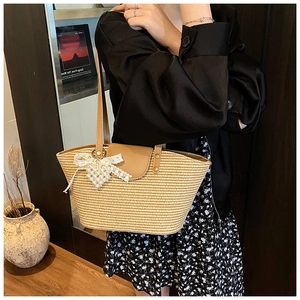 Close-up of beige woven straw tote bag with brown leather handles and a lace pearl charm