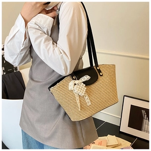 Detail of hand-woven beige straw tote with black leather flap and pearl bow accent