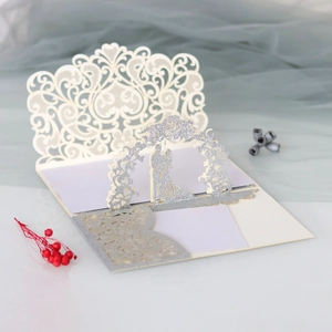 Detail of laser-cut lace wedding invitation with silver glitter 3D bride and groom