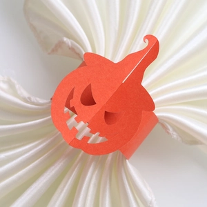 Close-up of orange laser-cut Jack-o'-lantern paper napkin ring on white satin fabric