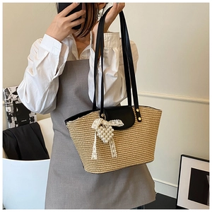 Detail of hand-woven straw tote bag with black leather handles and pearl heart pendant