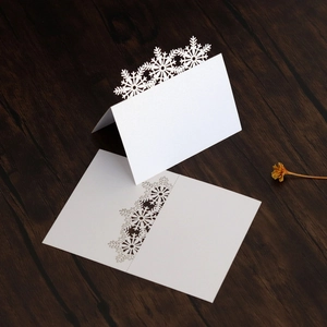 Laser-cut snowflake place cards in pearl white paper on a dark wooden background